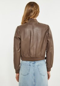 Brun læder bomberjakke med ribbede manchetter, cropped design og glat tekstur. Matchet med en lyseblå denimskørt.