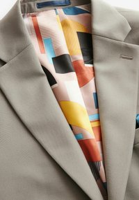 Blazer gris claro con tejido suave, con un forro de patrón geométrico colorido en tonos de rosa, azul, amarillo y acentos en negro.
