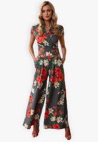 Floral jumpsuit in black with red and white flowers. Features a wrap design, short sleeves, wide legs, and pockets. Smooth fabric texture.