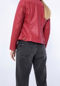 Červená kožená prošívaná bunda se štíhlým střihem, zdobená zlatými kovovými doplňky, v kombinaci s volně střiženými tmavě šedými džínami.