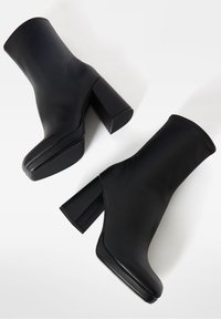 Paire de bottines noires à talons carrés et texture lisse, positionnées côte à côte sur fond blanc.