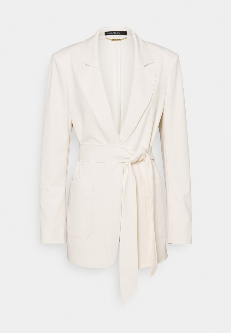 Blazer femme écru avec manches longues, revers crantés, deux poches avant et ceinture en tissu nouée à la taille.