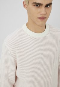 Pull en tricot rose clair avec une texture côtelée et un col rond blanc. Design près du corps mettant en valeur le tissu doux du vêtement.