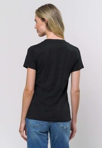 Črna bombažna majica s kratkimi rokavi, okroglim izrezom in gladko teksturo, v kombinaciji z ohlapnimi modrimi kavbojkami iz jeansa.