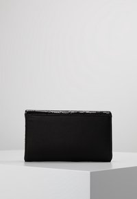 Svart rektangulär clutch med en slät tygyta och en subtil glänsande kant längs den övre kanten, placerad på en vit pedestal.