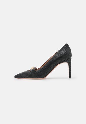 Chaussure à talon haut noire à bout pointu avec motif embossé, talon aiguille fin et boucle décorative dorée sur le dessus devant.
