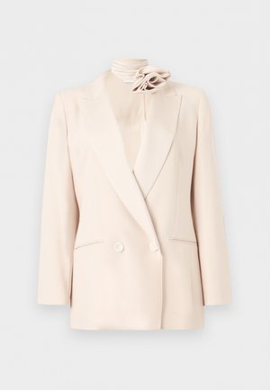 Crème dubbelbreasted blazer met inkeping in de revers, twee voorzakken, en een bijpassend crème bloemenaccessoire bij de hoge kraag.