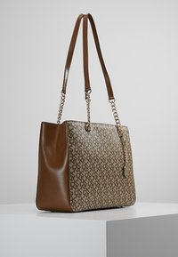 Taška na rameno s hnědou koženou základnou a vzorovanou textili í. Má dlouhé popruhy a zlatý řetězový akcent s přívěskem.