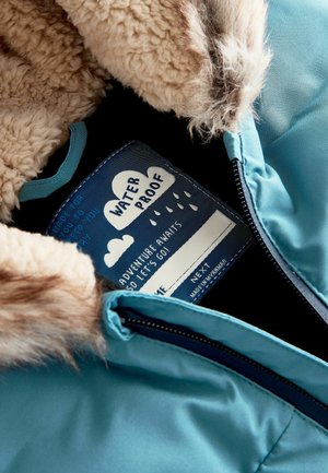 Innentuch einer hellblauen, wasserdichten Jacke mit einer samtigen, cremefarbenen Kunstfellfütterung. Das Etikett zeigt "WASSERDICHT" und verspielte Wolgrafiken. Reißverschlussdetails sind sichtbar.