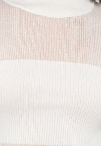 Pletene pulover v beli in breskvičasti črtasti zasnovi. Ima strukturirano, rebrasto obliko in visok vrat, iz mehkega in lahkega materiala.