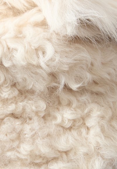 Fibres de laine douces, bouclées, de couleur crème, densément compactées, présentant des variations de texture allant de boucles serrées à des mèches lâches.