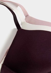 Sujeción con una base burdeos oscuro, con tirantes de color bloqueados en rosa claro y crema, y una textura de tela general suave.