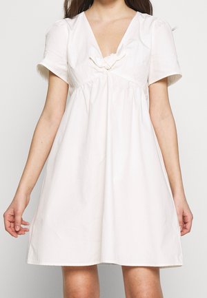Vit bomulls klänning med korta ärmar, V-ringning och samlad midja. Har en knutdetalj vid bröstet och en utställd nederkant.