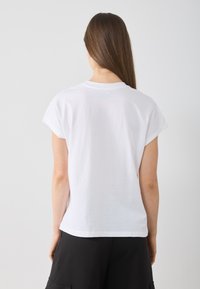 T-shirt en coton blanc avec un col rond et des manches courtes tombantes, présentant une coupe décontractée et un ourlet droit.
