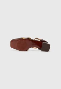 Chaussure à talons hauts en cuir marron avec des accents dorés et une semelle marron texturée. Elle présente un bout rond et une bride de cheville.