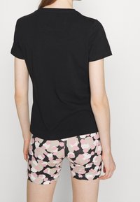 Czarny bawełniany t-shirt z krótkim rękawem, w połączeniu z szortami w wielokolorowy wzór z abstrakcyjnymi różowymi i kremowymi kształtami na czarnym tle.