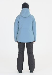 Blå vattentät jacka med huva, kombinerad med svarta snöbyxor. Slät textur, har artikulerade ärmar och en elegant design.
