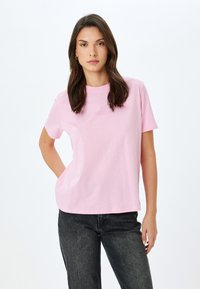 Camiseta de algodón rosa de manga corta, con el texto "Creativo" en una fuente sutil. Combinada con jeans de mezclilla oscura. Textura suave.
