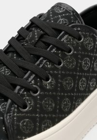 Sneaker nera in pelle verniciata testurizzata con un motivo geometrico, lacci neri piatti e suola in gomma bianca. Occhielli per la chiusura.