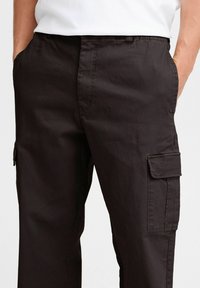 Schwarze Cargo-Hosen aus glattem Stoff, mit Seitentaschen und lockerer Passform. Merkmale sind ein Knopfverschluss und Gürtelschlaufen.
