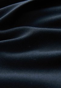 Tissu bleu foncé avec des plis doux et une texture fine visible sous un éclairage tamisé.