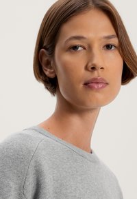 Grauer Strickpullover mit Rundhalsausschnitt und subtiler Textur. Das Model hat kurze Haare und einen neutralen Hintergrund.