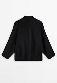 Veste noire à coupe décontractée, avec un ourlet et des poignets côtelés, un col élégant et une texture lisse. La vue arrière montre des lignes simples et épurées.