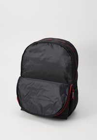 Fekete nylon hátizsák lekerekített formával, piros cipzárakkal és egy elülső zsebbel. Simának tűnő textúrával és párnázott oldalakkal a kényelem érdekében.