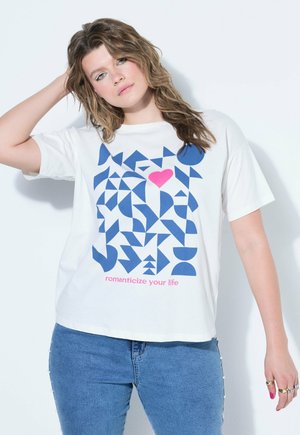 Junge Frau mit welligem Haar trägt ein weißes T-Shirt mit blauen geometrischen Formen, einem pinkfarbenen Herz und dem Text „romanticize your life“, kombiniert mit blauen Jeans.