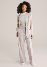 Šviesiai rožinis pritaikytas kostiumas su vieno mygtuko švarku ir klostuotomis plačiomis kelnėmis. Po apačia dėvimas tekstūruotas šviesiai pilkas marškinėlis. Baltos sportbačiai.