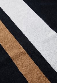 Asciugamano a strisce con sezioni nere, bianche e tan. Texture morbida con tessuto peloso, e blocchi di colore chiaramente definiti che si estendono orizzontalmente.