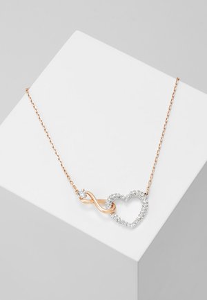 Collana a catena in oro rosa con simbolo di infinito e cuore adornati da cristalli trasparenti, su uno sfondo grigio minimalista.