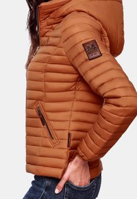 Hnědá prošívaná bundička s horizontálním prošíváním, zipovou boční kapsou a nášivkou s logem na rukávu. Hladký povrch, přiléhavý střih.