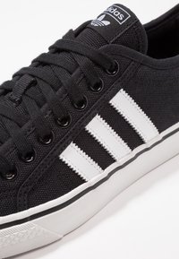 Svarta kanvas sneakers med vit tre-stripes design, svarta metallöglor och vit gummisula. Har en texturerad ovandel och logotagg.