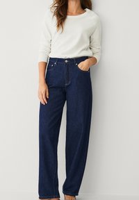 Jean bleu foncé taille haute avec une coupe droite, doté d'une fermeture à boutons, de poches avant et d'une texture en denim lisse.