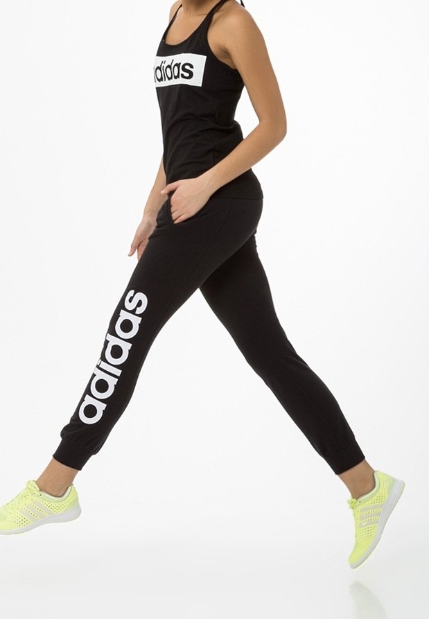 Czarny sportowy top na ramiączkach z białym logo "adidas", w zestawie z czarnymi joggerami z kieszeniami po bokach i białym nadrukiem "adidas", uzupełniony żółtymi butami sportowymi.