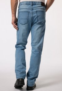 Světle modré denimové džíny s volným střihem, elastickým pasem a dvěma zadními kapsami. Nosené s černými botami, které ukazují hladkou texturu.