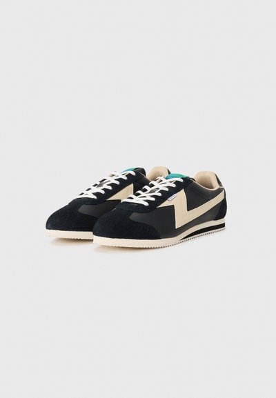 Black suede and fabric sneakers with a cream accent, featuring a triangular design, white laces, and a textured rubber sole.