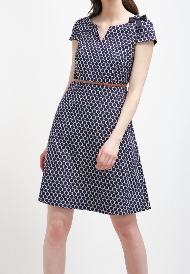 Vestido de marina con lunares blancos, tela suave, mangas de capucha, escote en V y detalle de lazo en el hombro, ceñido con un cinturón marrón en la cintura.