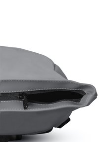 Geanta gri cu fermoar, cu o suprafață netedă și mată. Are un fermoar în partea de sus și un design plat, rotund. Interiorul este întunecat și texturat.
