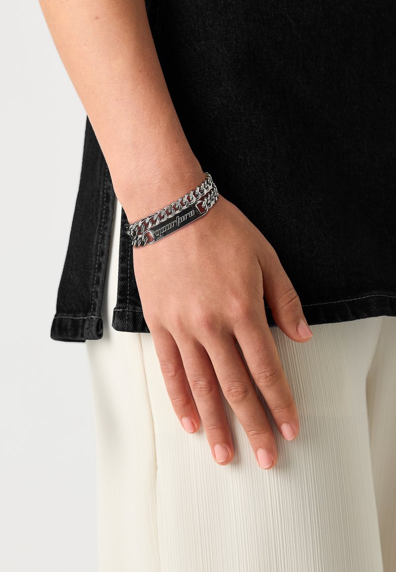 Silverfärgad kedjebracelet med en plan graverad platta, som har en slät metallisk finish och sammankopplad kedjedesign.