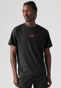 Tricou din bumbac negru, cu guler rotund și mâneci scurte, având un logo roșu Levi's proeminent centrat pe piept.