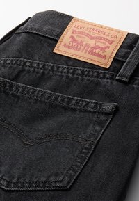 Vaqueros de mezclilla negra con una etiqueta de cuero que presenta el logo de Levi Strauss & Co. La tela tiene una textura suave y detalles de costura clásicos.