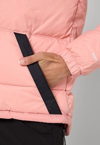 Rosa vadderad jacka med ribbad struktur, marinblå sidoficka och elastiska muddar. Har en lätt design som passar för lager-på-lager.