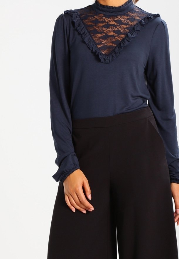 Mörkblå långärmad tröja med spetsinsats, volangkrage och manschetter. Kombinerad med svarta vida byxor, vilket betonar kontrasten i texturer och färger.