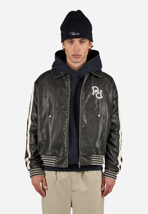 Black leather jacket with ribbed cuffs, striped white accents, and embroidered logo on chest. Worn over a dark hoodie and a beanie.