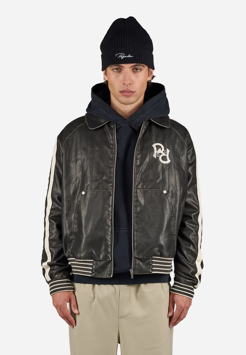 Zwarte leren jas met ribbels aan de mouwen, gestreepte witte accenten en geborduurd logo op de borst. Draagt over een donkere hoodie en een muts.