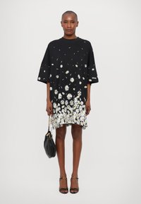 Sort kjole med et blomsterprint af hvide margueritter ved kanten. Korte ærmer, løs pasform og let asymmetrisk design.