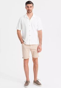 Chemise blanche à manches courtes avec un motif texturé, shorts beige roulés et chaussure à lacets grise. Design simple et palette de couleurs neutres.