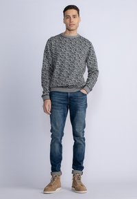 Pulover negru cu un model alb, guler rotund, mâneci lungi; asortat cu blugi albaștri și cizme de culoare chihlimbar cu șiret. Textură netedă.